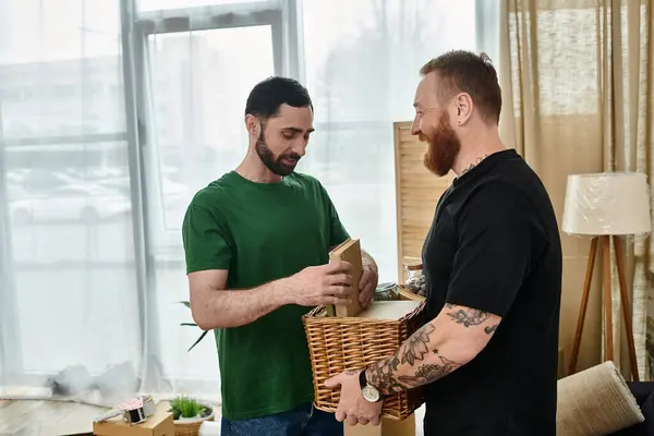 Two men, a gay couple in love, stand next to each other in their new living room surrounded by moving boxes. — Stock Photo