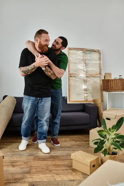 Um casal gay apaixonado, cercado por caixas móveis, está lado a lado em sua sala de estar de sua nova casa. — Fotografia de Stock
