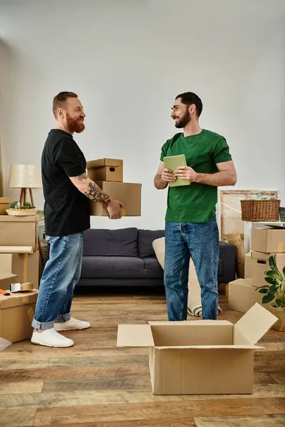 A gay couple stands side by side in a room filled with moving boxes, signaling a fresh start in their new home. — стоковое фото