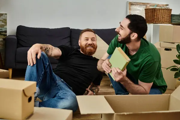 Ein paar Männer, ein schwules Paar, entspannen sich auf Kisten in ihrem neuen Zuhause, umgeben von Umzugskartons als Zeichen eines neuen Kapitels. — Stockfoto