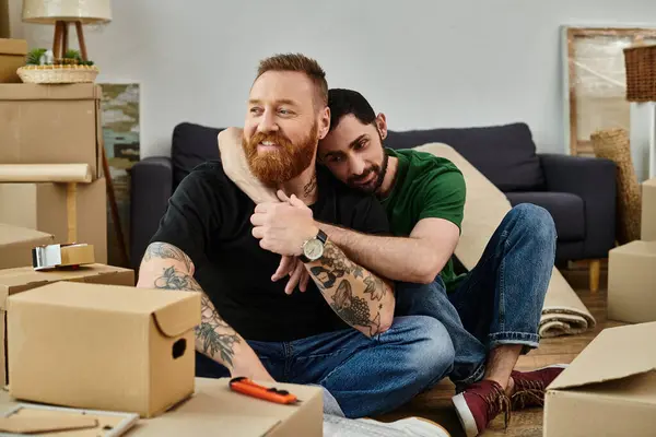 A gay couple in love, seated on boxes, embrace the start of a new life in their new home amidst the relocation process. — Stock Photo