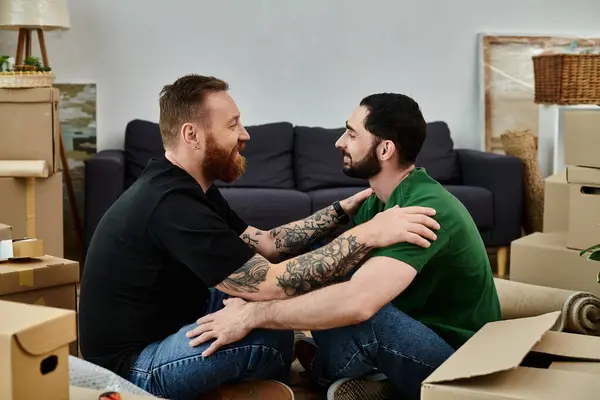 A gay couple in love sits together on stacked boxes, symbolizing a new chapter in their lives as they move into their new home. — Stock Photo