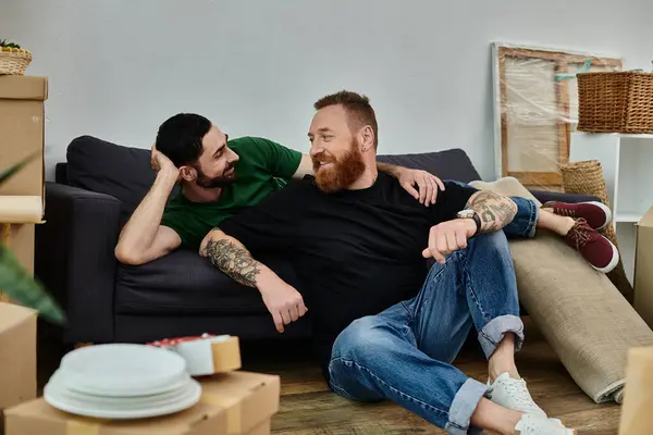 Um casal gay relaxa junto em cima de um sofá em sua nova casa, cercado por caixas descompactadas, marcando o início de um novo capítulo. — Fotografia de Stock