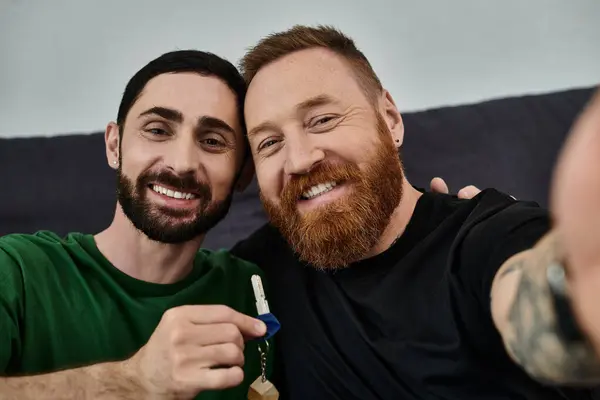 Dos hombres enamorados disfrutan de un momento divertido tomando una selfie junto con una llave en su nuevo hogar. - foto de stock