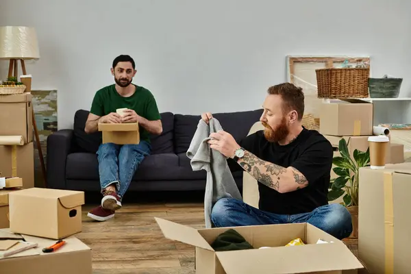 A gay couple in love relaxes on the couch in their new home, surrounded by moving boxes, embracing their fresh start. — Stock Photo