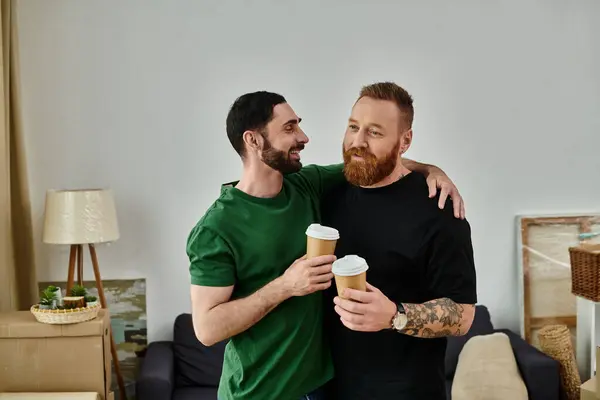 Deux hommes, un couple gay, se tiennent ensemble au milieu de boîtes mobiles dans leur nouvelle maison, partageant un moment d'amour et d'anticipation. — Photo de stock