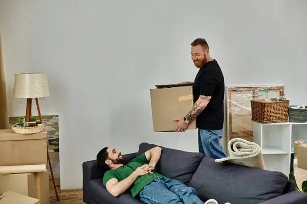 Um homem encontra-se confortavelmente em um sofá em uma sala de estar cheia de caixas móveis, em meio à emoção de começar um novo capítulo na vida. — Fotografia de Stock
