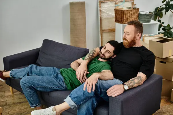 Un couple gay se détendre sur un canapé au milieu de leurs tâches de déménagement, exsudant le confort partagé et la compagnie. — Photo de stock