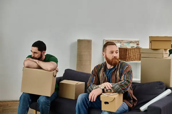 A gay couple sit atop a couch amidst moving boxes, having disagreement in their new home. — Stock Photo