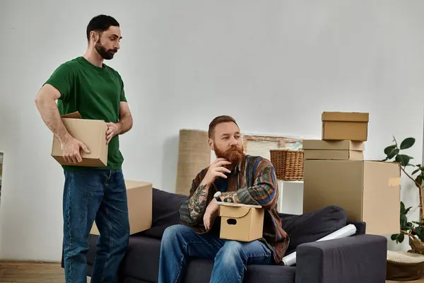 A man sits on a couch surrounded by boxes, reflecting on his new beginnings in a new home with his partner. — Stock Photo