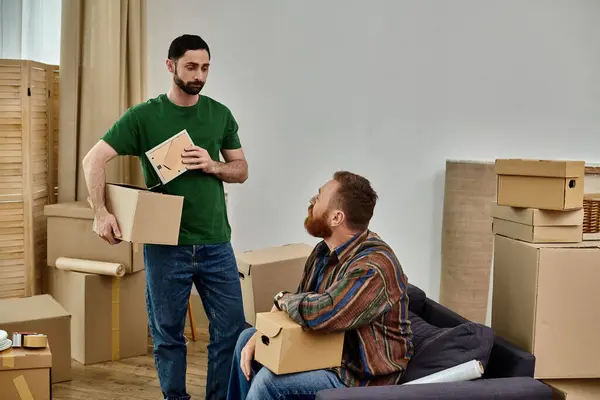 Um homem está ao lado de seu parceiro, segurando caixas enquanto se preparam para se mudar para uma nova casa cheia de amor. — Fotografia de Stock
