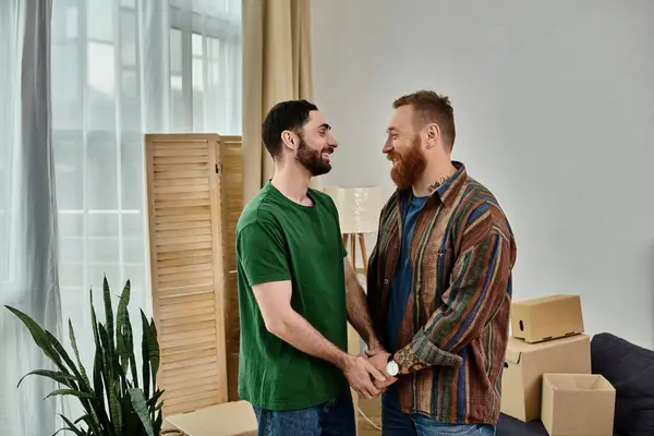 Gay casal no amor fica por cada outros no um sala de estar preenchido com em movimento caixas, começando um novo capítulo no seu vida juntos. — Fotografia de Stock