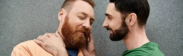 A portrait of a gay couple in casual attire, standing side by side against a grey wall. — Stock Photo