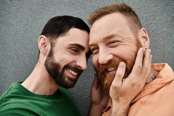 Due uomini innamorati sorridono e posano per un ritratto contro un muro grigio, irradiando felicità e insieme. — Foto stock