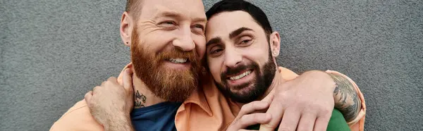 A portrait of a gay couple standing next to each other, exuding love and solidarity against a grey wall. — Stock Photo