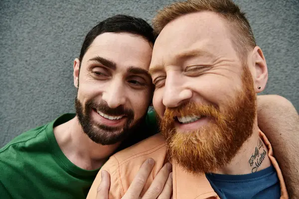 A gay couple in casual attire standing affectionately next to each other against a grey wall, radiating love and harmony. — Stock Photo
