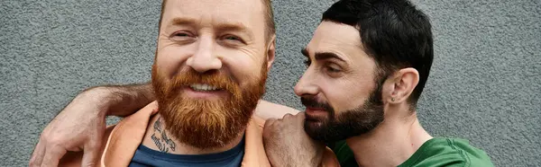 Dois homens, um casal gay, estão amorosamente juntos em trajes casuais contra uma parede cinza. — Fotografia de Stock