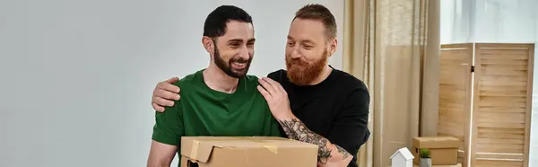 Два чоловіки, частина люблячої гей-пари, стоять поруч, тримаючи коробку в своєму новому будинку — стокове фото