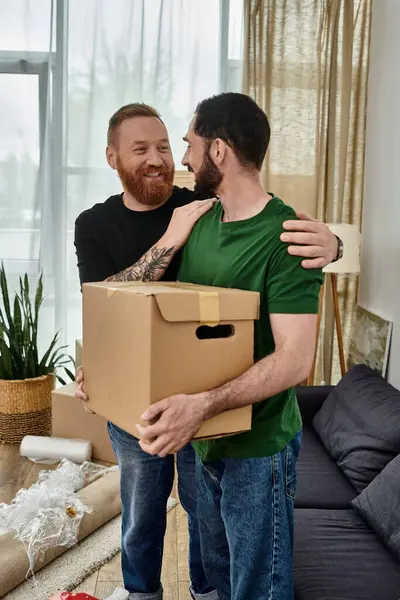 Deux hommes, un couple gay amoureux, partagent un moment de calme dans leur nouveau salon au milieu de boîtes mobiles. — Photo de stock