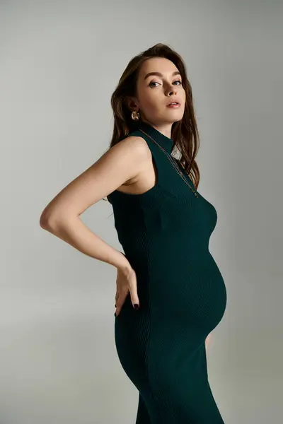 A radiant pregnant woman in a flowing green dress showcasing her baby bump with grace and elegance. — Stock Photo