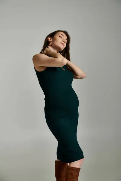 A young pregnant woman elegantly stands in a green dress, exuding grace and charm. — Stock Photo