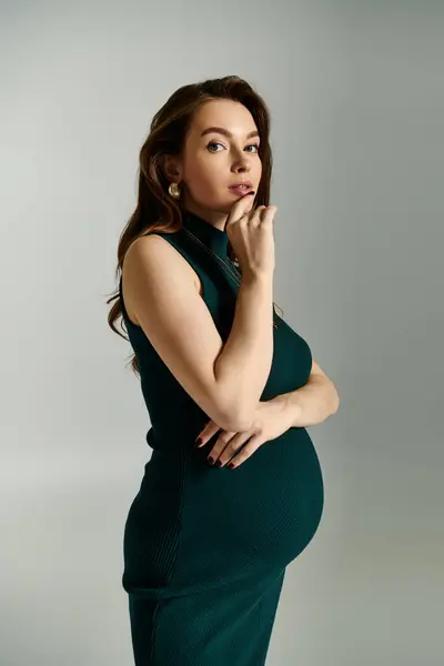 A young pregnant woman in a green dress exudes confidence while posing gracefully for a portrait. — Stock Photo