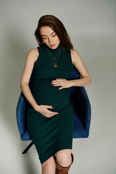 Una mujer embarazada se encuentra elegantemente en un vestido verde y botas marrones. - foto de stock