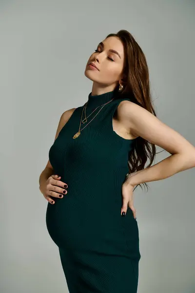 Молода, вагітна жінка в зеленій сукні витончено позує на портрет, виключаючи елегантність і впевненість. — стокове фото