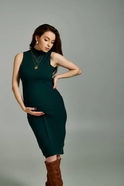 Una giovane donna incinta elegantemente vestita con un abito verde fluente ed eleganti stivali marroni. — Foto stock
