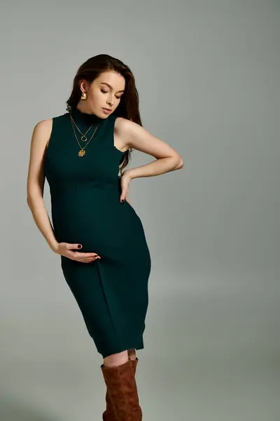 Una joven embarazada elegantemente vestida con un vestido verde fluido y elegantes botas marrones. - foto de stock