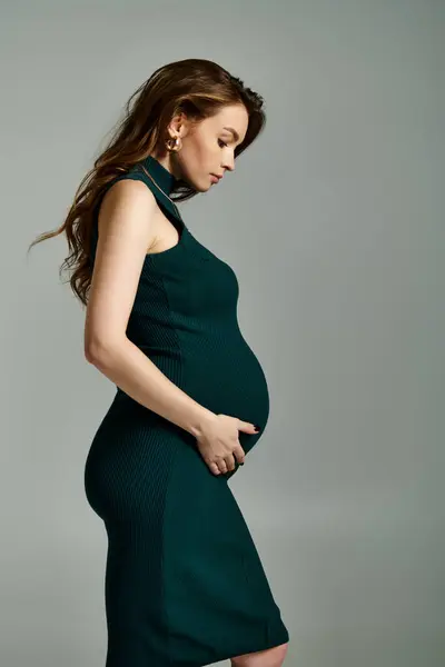 Светящаяся беременная женщина в элегантном зеленом платье излучает радость и предвкушение. — стоковое фото