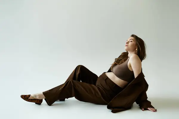 Pregnant woman in black top and brown pants sits elegantly on the ground. — Stock Photo