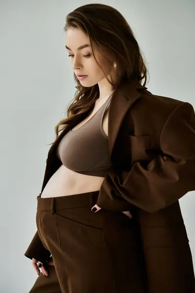 A young pregnant woman in a stylish brown suit poses confidently against a neutral grey background. — Stock Photo