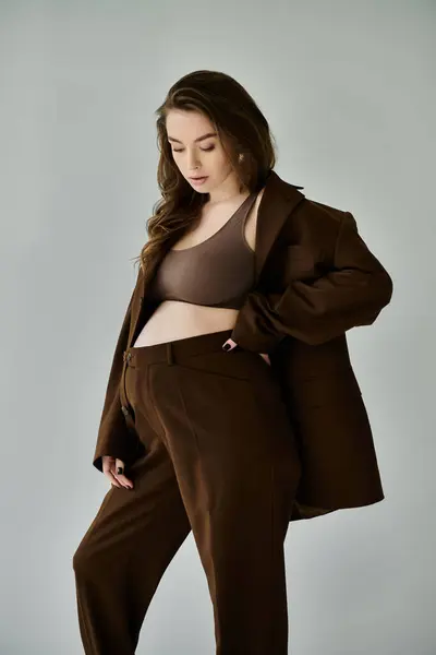 Una giovane donna incinta posa elegantemente in un abito marrone con una giacca su uno sfondo grigio neutro. — Foto stock