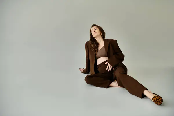 A pregnant woman in a brown suit sits peacefully on the floor — Stock Photo