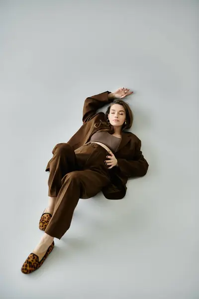 A serene young pregnant woman in a sophisticated brown outfit lounging gracefully on the ground. — Stock Photo
