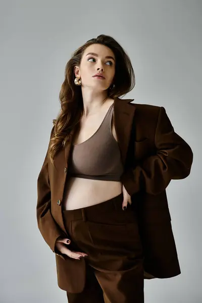A young pregnant woman in a brown suit with a blazer striking a confident pose on a grey background. — Stock Photo