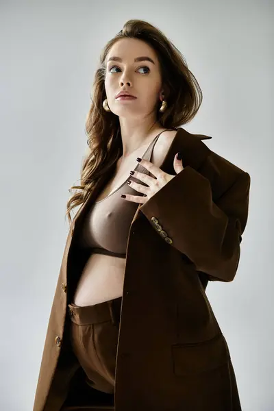 A stylish young pregnant woman in a brown suit with a blazer striking a pose against a grey background. — Stock Photo