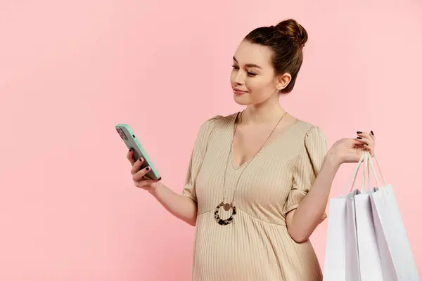 Une jeune femme enceinte en robe tenant un téléphone portable et des sacs à provisions. — Photo de stock