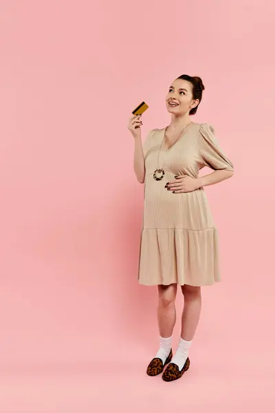 Pregnant woman in elegant dress holds credit card symbolizing modern motherhood. — Stock Photo