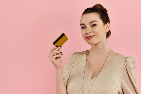 Uma mulher grávida elegantemente segura um cartão de crédito em sua mão contra um pano de fundo rosa. — Fotografia de Stock