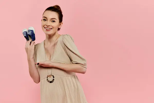 A young pregnant woman in a dress holds pair of baby shoes, showcasing her anticipation and joy for the future. — Stock Photo
