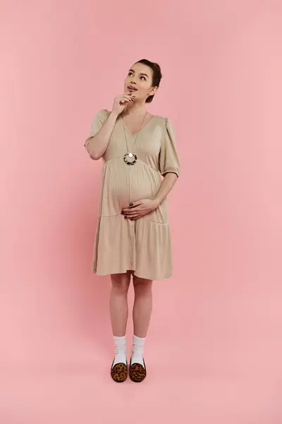 Jovem grávida de pé com confiança em um vestido fluindo contra um fundo rosa vibrante. — Fotografia de Stock