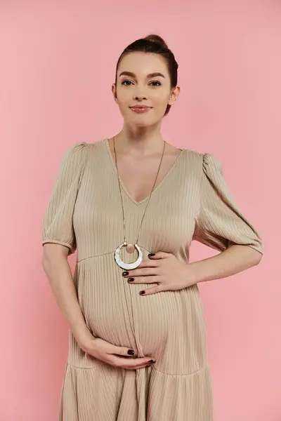 A young pregnant woman in a flowing dress poses elegantly for a shot against a vibrant pink backdrop. — Stock Photo