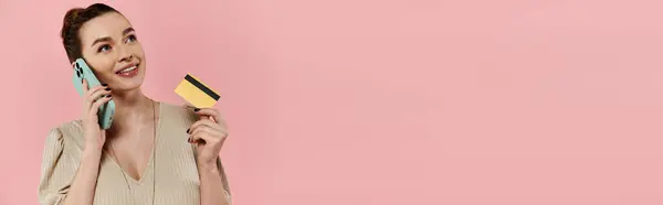 A young pregnant woman elegantly holds a credit card and cell phone against a pink background, ready to make a purchase. — Stock Photo