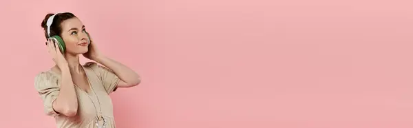 Una joven embarazada en un vestido habla pacíficamente en su teléfono celular sobre un fondo rosa. - foto de stock