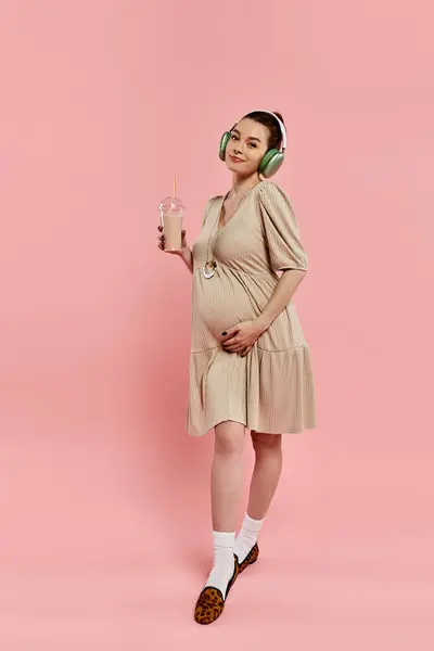 Une femme enceinte dans une robe écoute paisiblement de la musique et tient un verre — Photo de stock