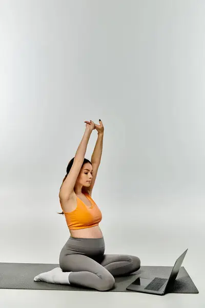 Молодая беременная женщина в активной форме сидит на коврике для йоги, руки подняты в воздухе в спокойной и мощной позе. — стоковое фото