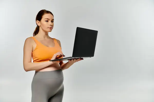A young, sporty pregnant woman in active wear holds a laptop computer in her hands. — Stock Photo