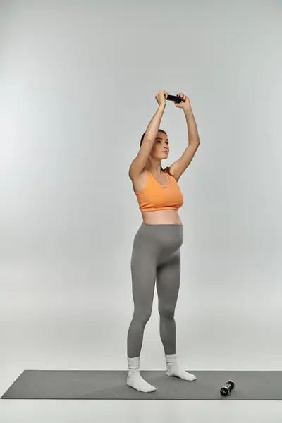 Eine schwangere Frau in Aktivkleidung steht mit erhobenen Händen auf einer Yogamatte und strahlt Gelassenheit und Anmut aus. — Stockfoto
